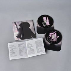 Music album packaging featuring a CD case, discs, and an information booklet with black and pink artwork.